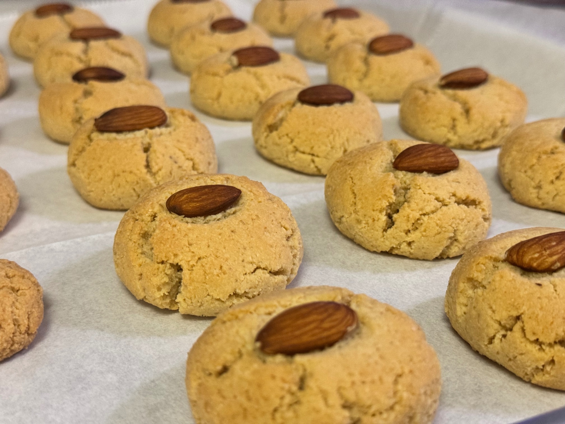 Rows of golden nankhatai cookies topped with whole almonds on parchment